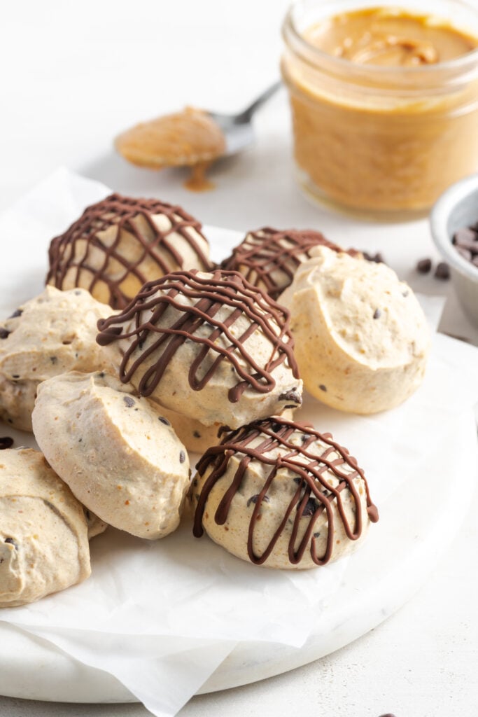 white marble round topped with parchment paper and a pile of greek yogurt frozen peanut butter balls.