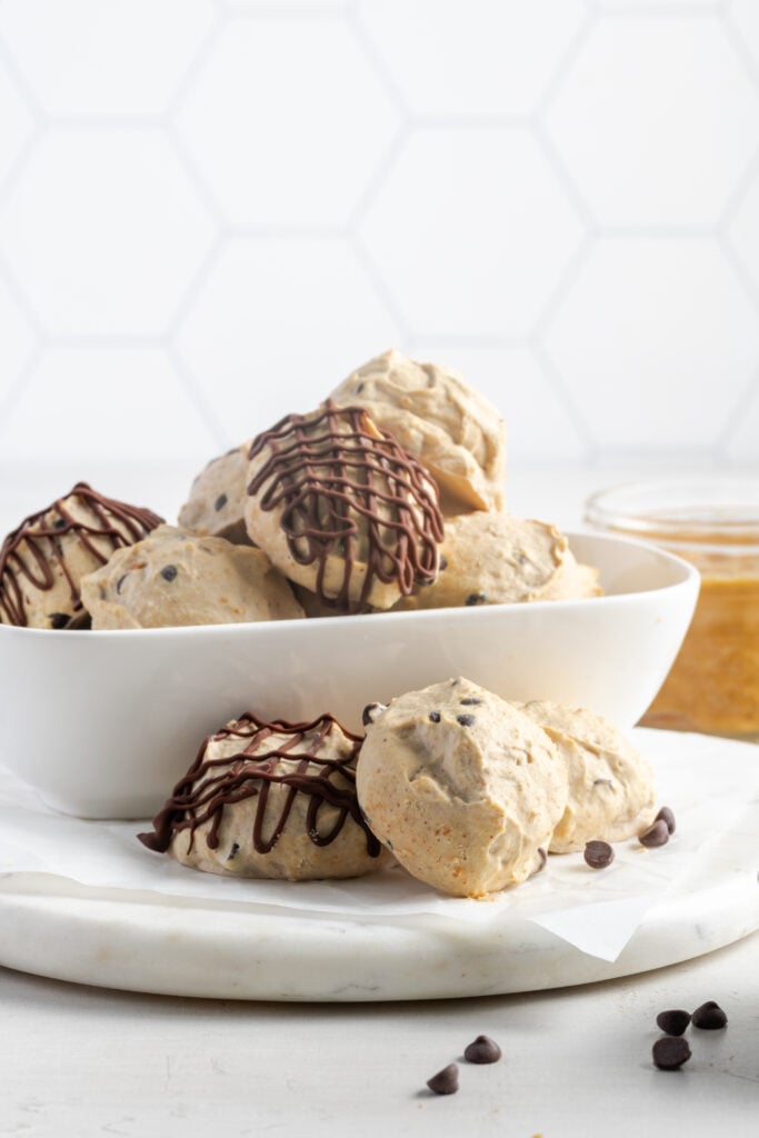 bowl of chocolate drizzled Greek yogurt chocolate chip peanut butter balls in front of a white hexagonal tile backsplash.
