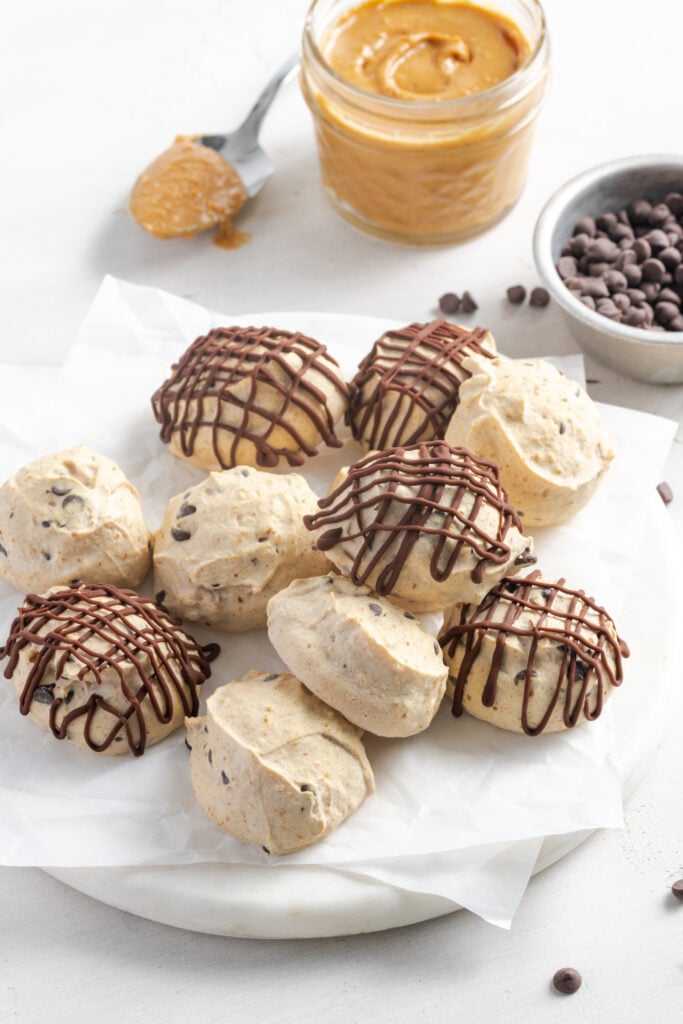 plate of frozen Greek yogurt peanut butter bites with a jar of peanut butter and a pinch bowl of chocolate chips.
