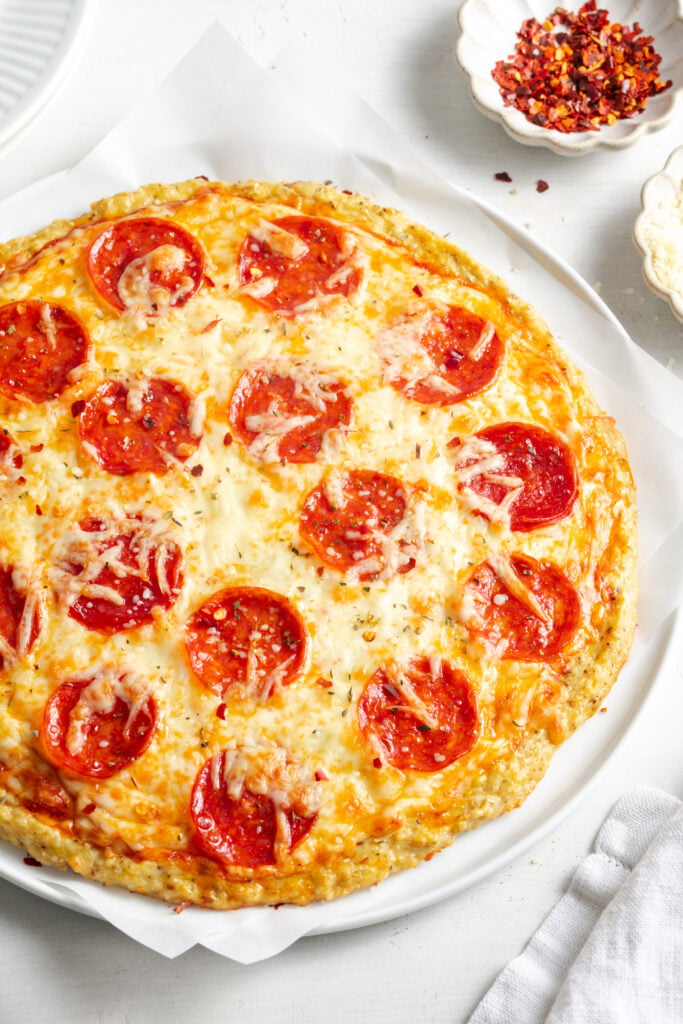 45 degree angle of ground chicken crust pizza with pepperoni and marinara sauce.