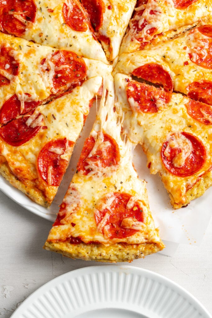 slice of pepperoni pizza with a chicken crust being pulled away from the rest, showing a stretchy mozzarella cheese pull.