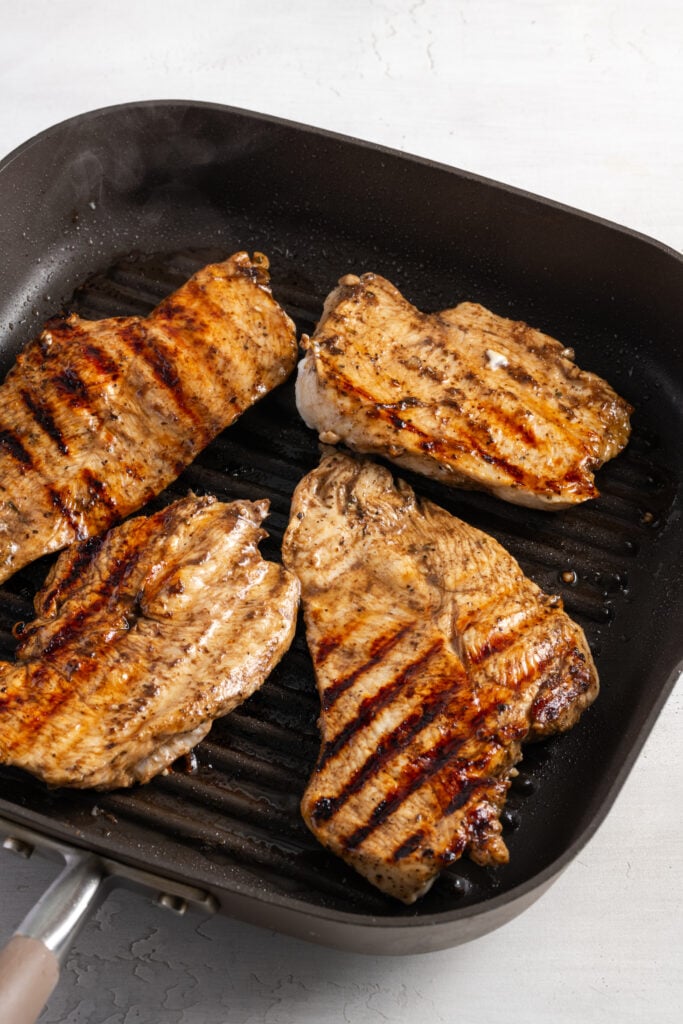 balsamic marinated chicken breasts cooking on a grill pan; they've been flipped so you can see the nice char marks.