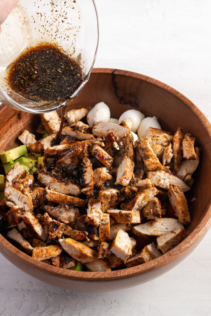 action shot of the reserved balsamic vinaigrette being poured atop the bowl of chopped chicken and fresh caprese salad ingredients.