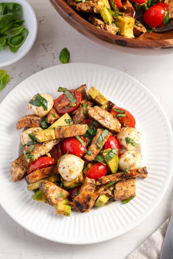 flat lay shot of fresh and healthy chicken caprese salad on a white dinner plate on a white table.