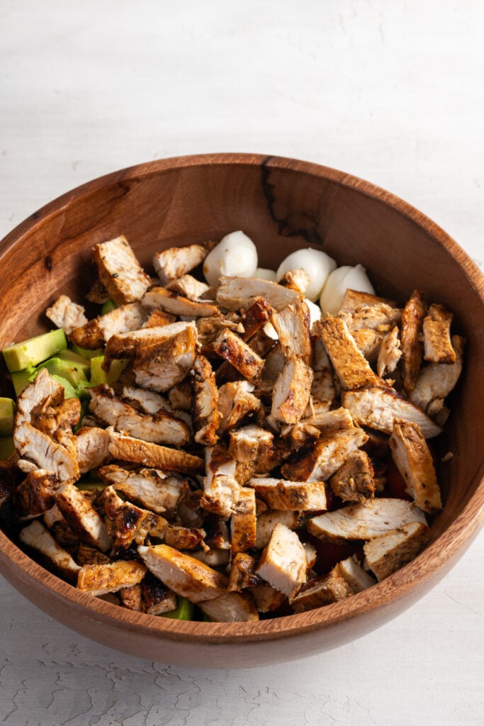 chopped cooked balsamic marinated chicken added to the bowl with the fresh ingredients.