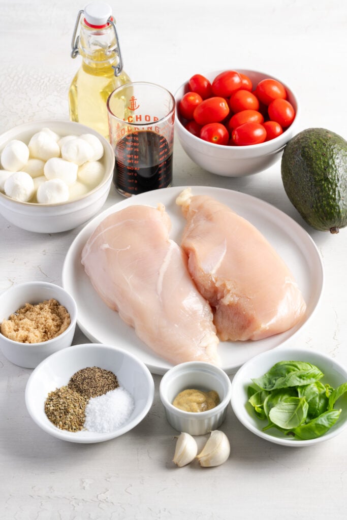 ingredients needed to make chicken caprese salad recipe measured out on white plates on a white table.