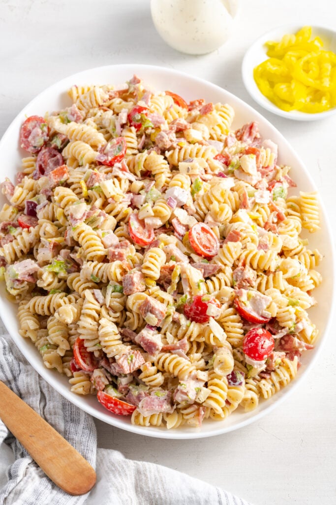 creamy grinder pasta salad in an oblong white serving bowl with a wooden serving spoon.