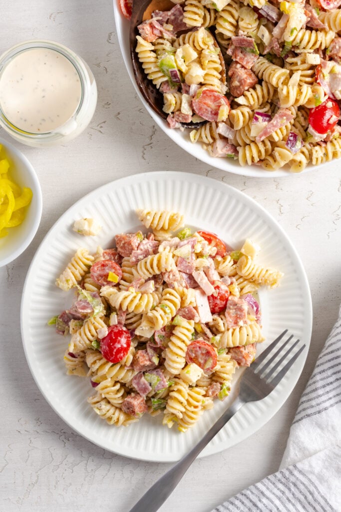 overhead shot of a serving of easy grinder pasta salad on a white plate on a white table with a silver fork.