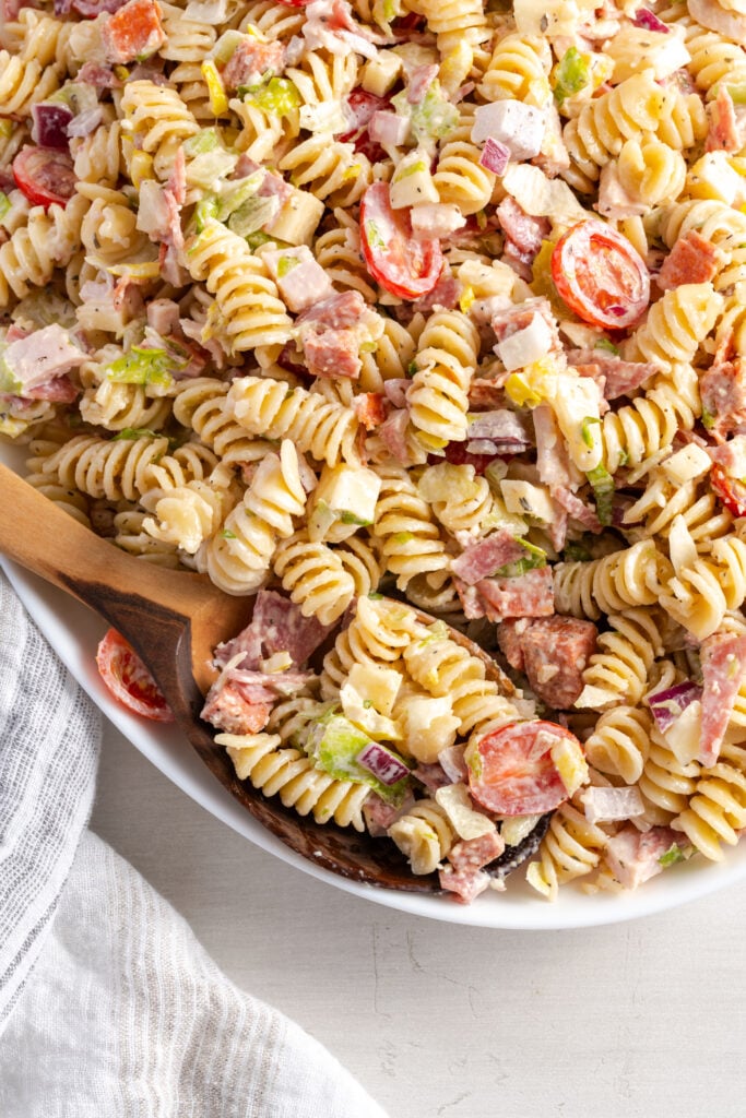 overhead closeup shot of a grinder sandwich inspired pasta salad with a wooden serving spoon taking a scoop.