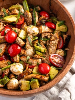 overhead closeup shot of a wooden salad bowl filled with chicken avocado caprese salad.