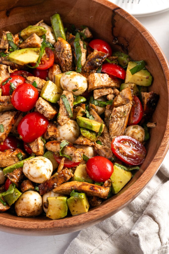 overhead closeup shot of a wooden salad bowl filled with chicken avocado caprese salad.