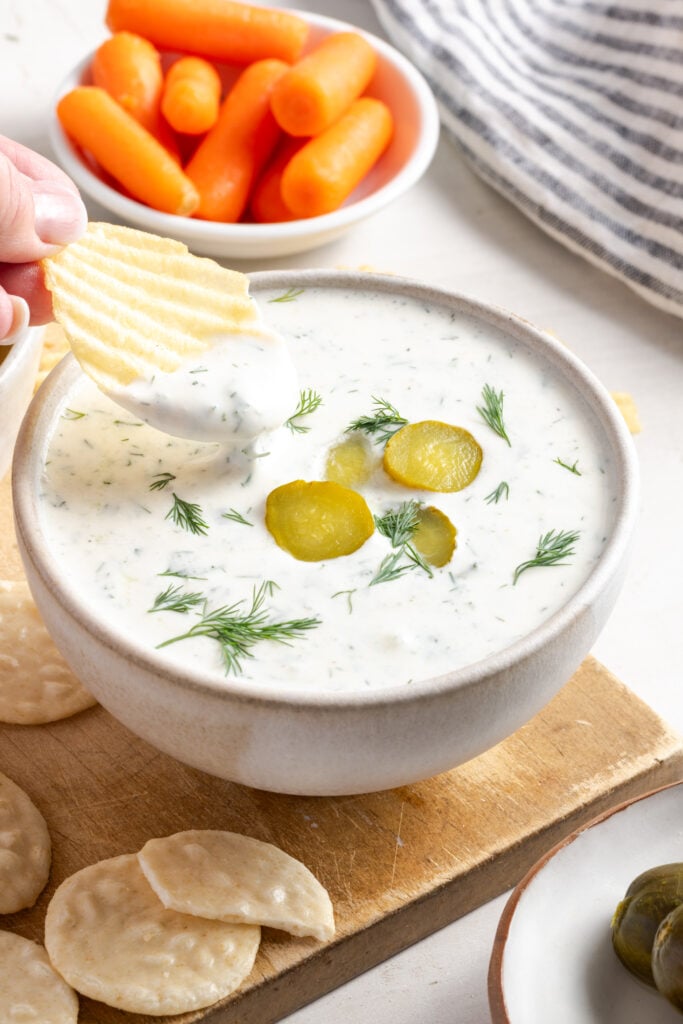 hand dipping a ridged chip into a bowl of tangy dill pickle dip made with cottage cheese and greek yogurt.
