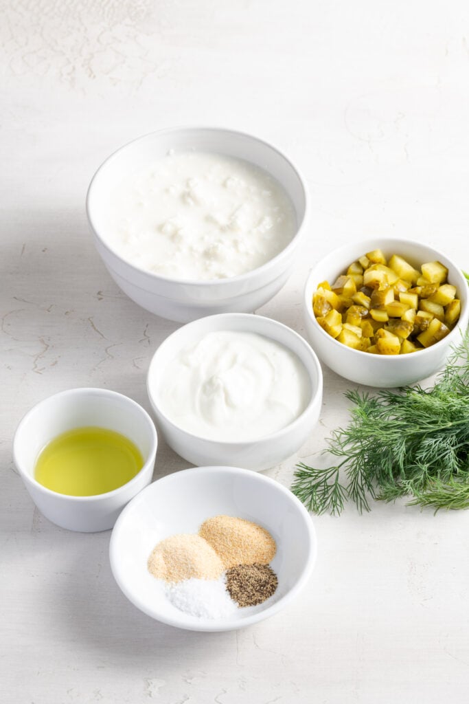 ingredients needed to make healthy high protein dill pickle dip recipe measured out on a white table.