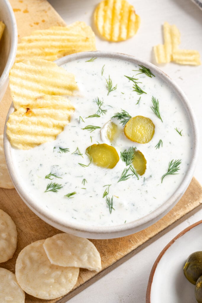 potato chips in a white bowl of high protein healthy dill pickle dip.