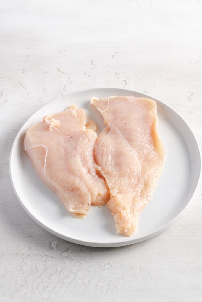 raw chicken breast pounded out to 1/2 inch thickness on a white plate.