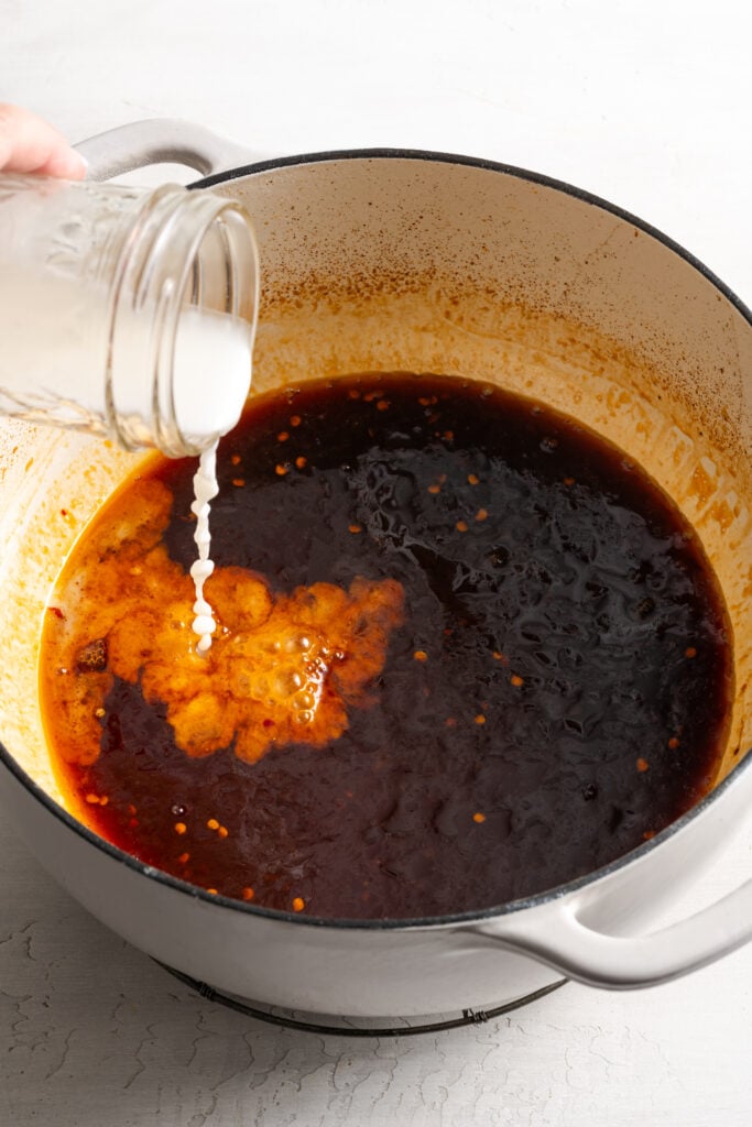 action shot of the cornstarch slurry being added to the pan with the sesame marinade and braising liquid.