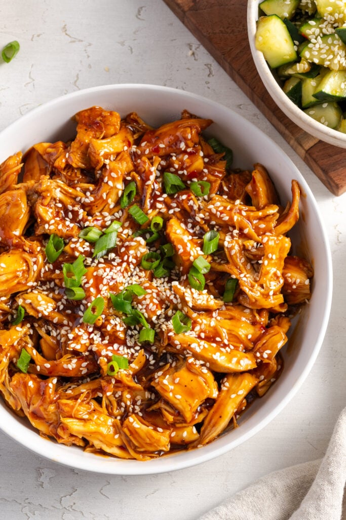 overhead closeup shot of easy shredded sesame chicken topped with scallions and sesame seeds on a white table.