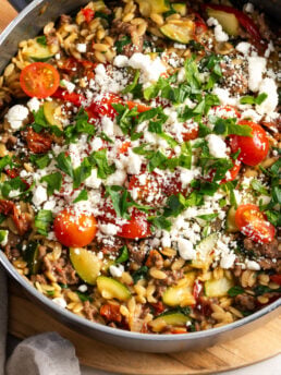 closeup shot of a greek beef orzo skillet topped with feta, herbs, and cherry tomatoes.
