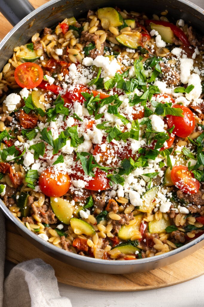 closeup shot of a greek beef orzo skillet topped with feta, herbs, and cherry tomatoes.