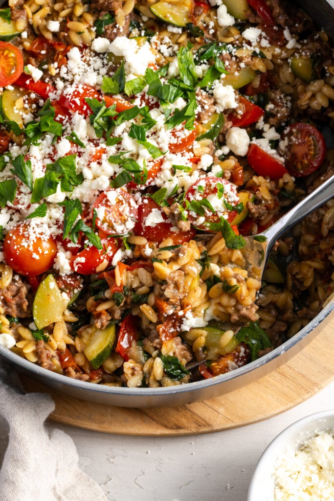 serving spoon dipped into the greek inspired ground beef orzo skillet for plating.