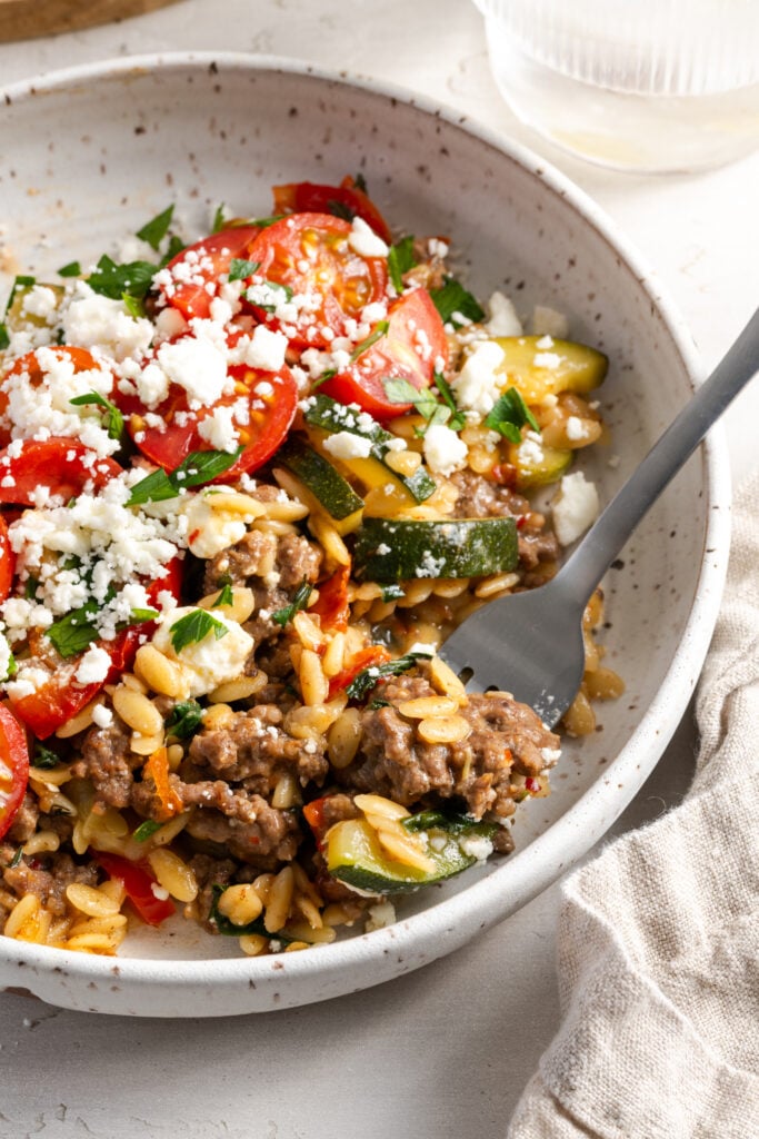 silver fork taking a bite of ground beef and orzo skillet.