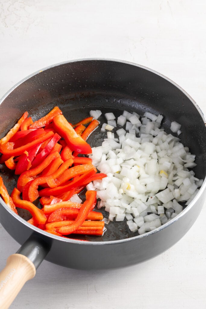 chopped onions and sliced peppers added to a skillet with oil for sautéing.