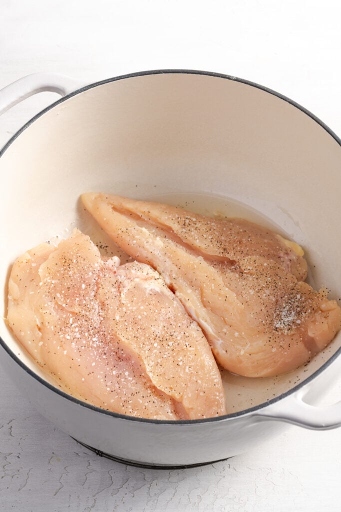 seasoned chicken breasts being seared in a large white dutch oven.