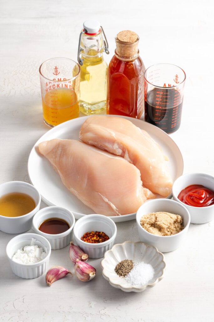 ingredients needed to make healthy shredded sesame chicken rice bowls measured out on a white table.